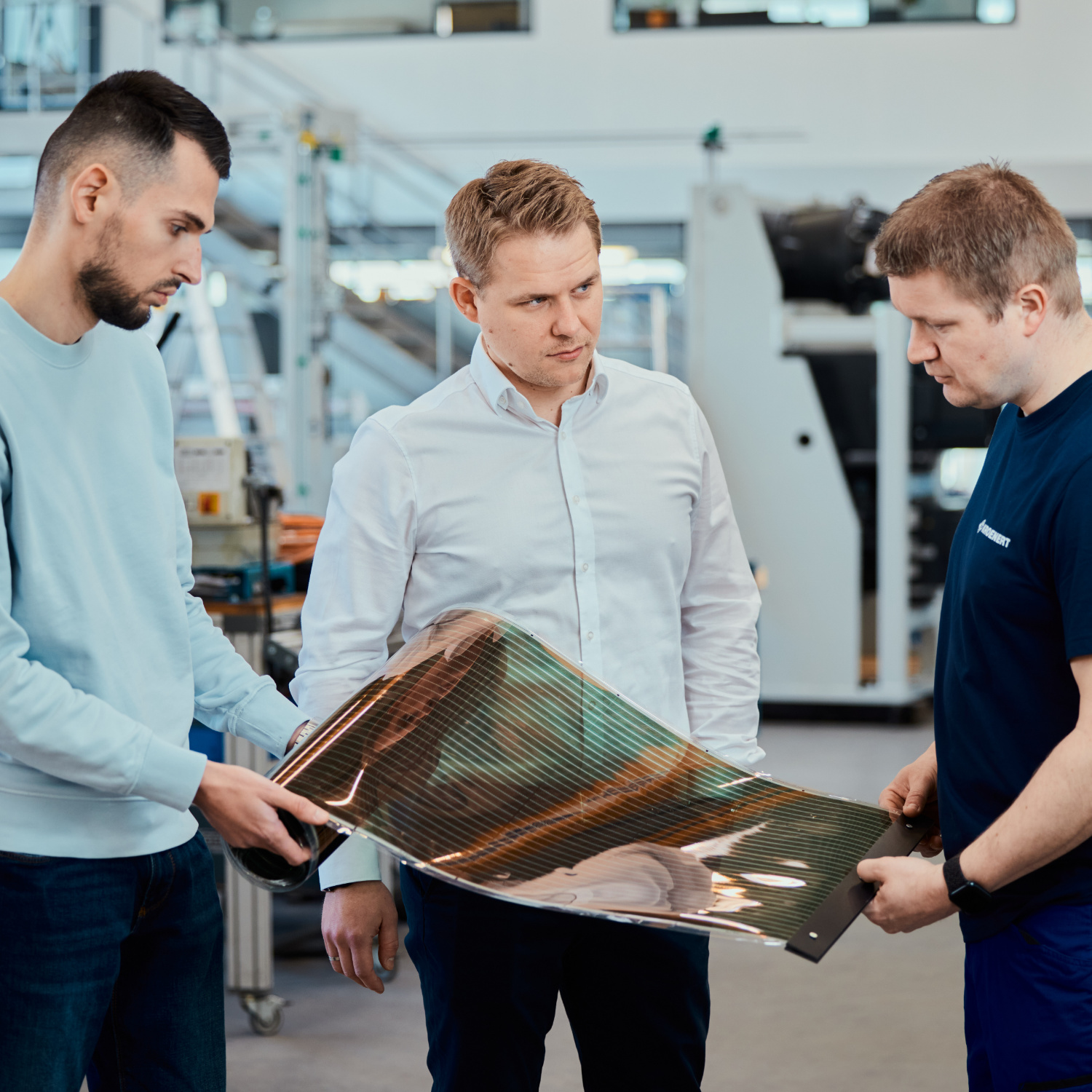 Three people are standing together in the assembly hall with organic solar cells.